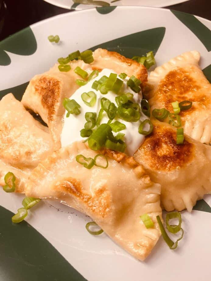 close up of pan fried potato and cheese pierogi topped with sour cream and green onions.