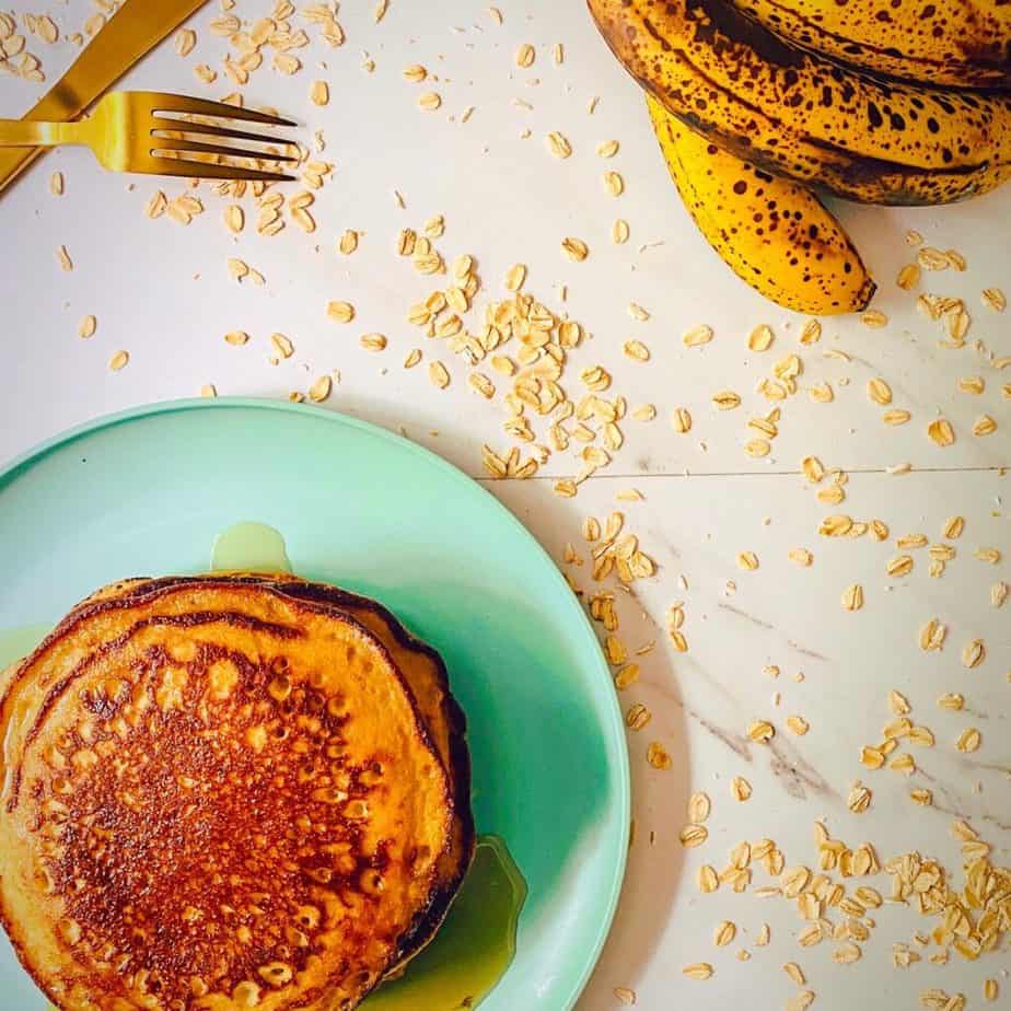 Overhead shot of my healthy banana blender pancakes with oats strewn about, gold flatware and speckled bananas