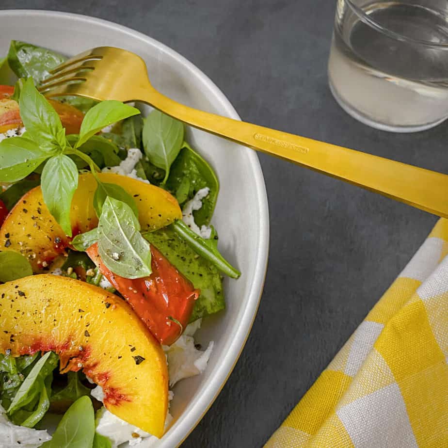 peach tomato burrata salad with a glass of pinot grigio, gold colored fork, and my favorite yellow gingham napkin.