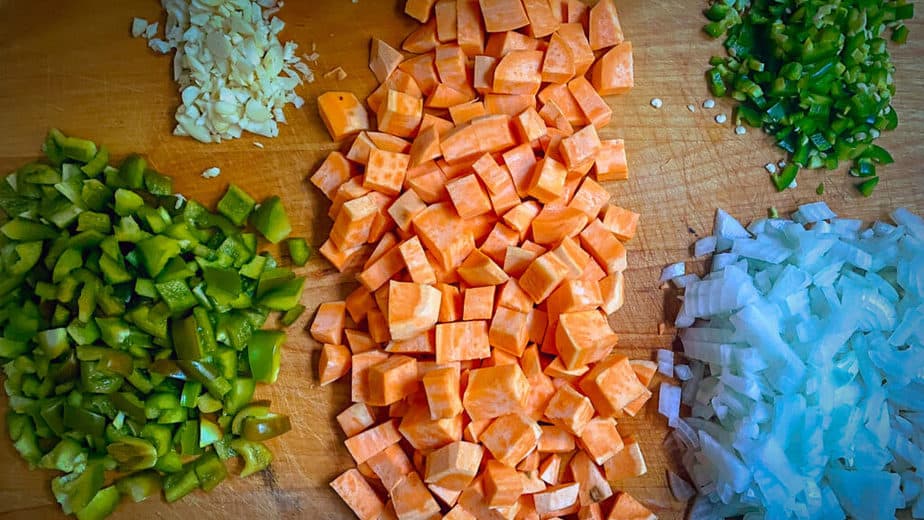 Minced garlic, diced green bell pepper, diced sweet potatoes, minced jalapeno and diced onion on cutting board