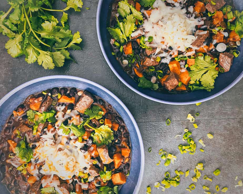 Two bowls of steak chili shot overhead with bunch of cilantro and green onions decorating shoot surface