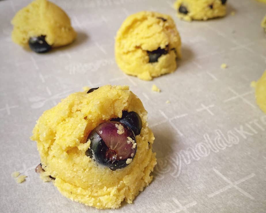 An up-close shot of scooped dough with blueberries on a parchment lined sheet