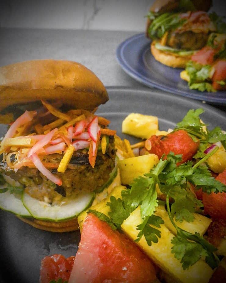 Final image of pork banh mi burger with spicy pineapple watermelon salad on a grey plate on a light grey counter with a white marble backsplash