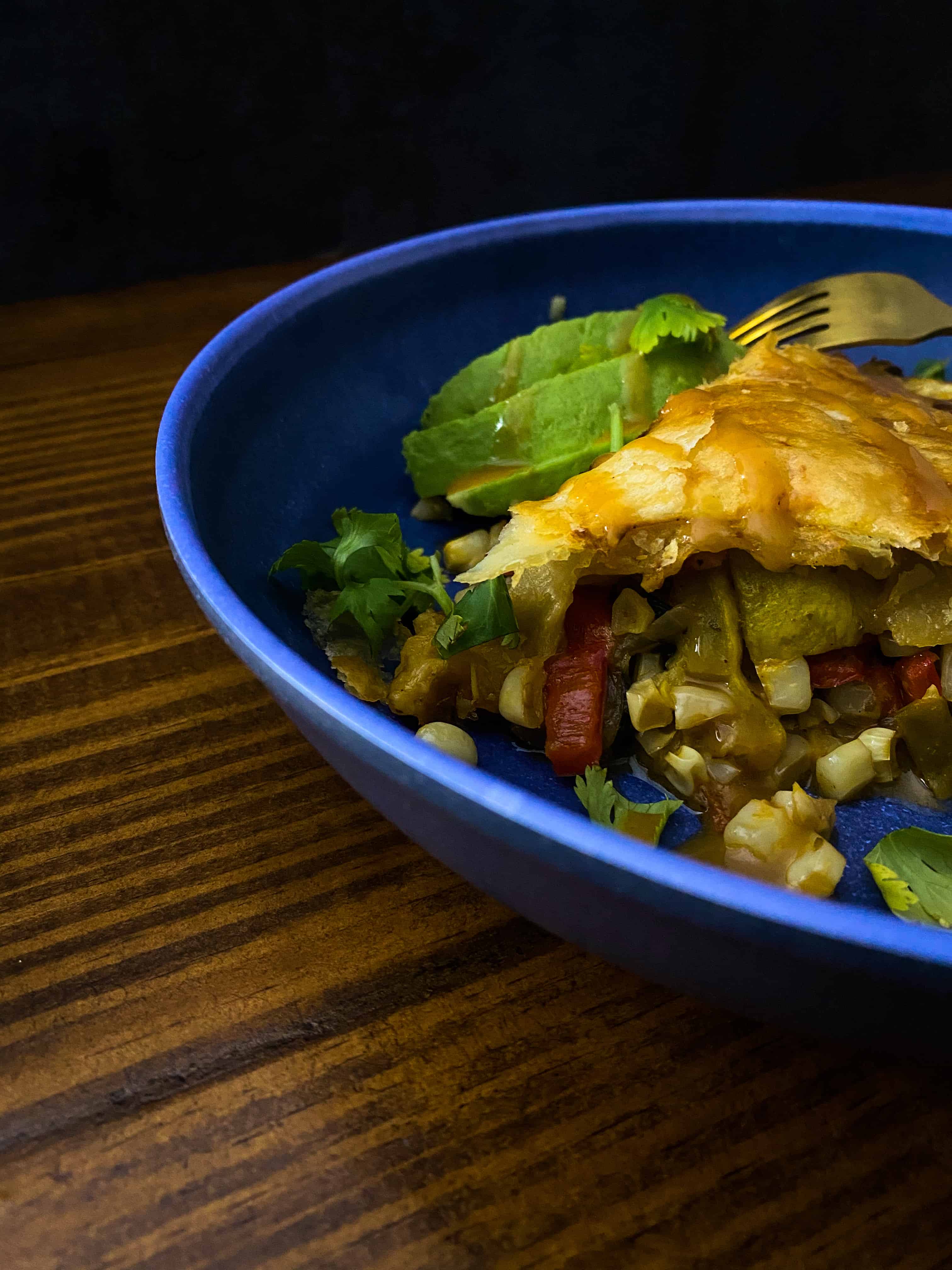 A 45 degree angle shot of a slice of my calabacitas pot pie, with all kinds of vegetable goodness spilling out the side. Garnished with avocado, cholula and cilantro