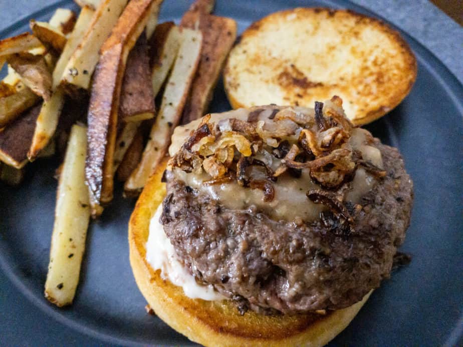 A close up shot of the French Dip Burger with Homemade French Fries, Garlic Mayonnaise, Black Pepper Gravy and Crispy Shallots on a grey plate.