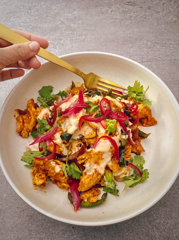 Slightly angled overhead close-up of the Yucatan Citrus Chicken bowl with my hand holding a gold colored fork.