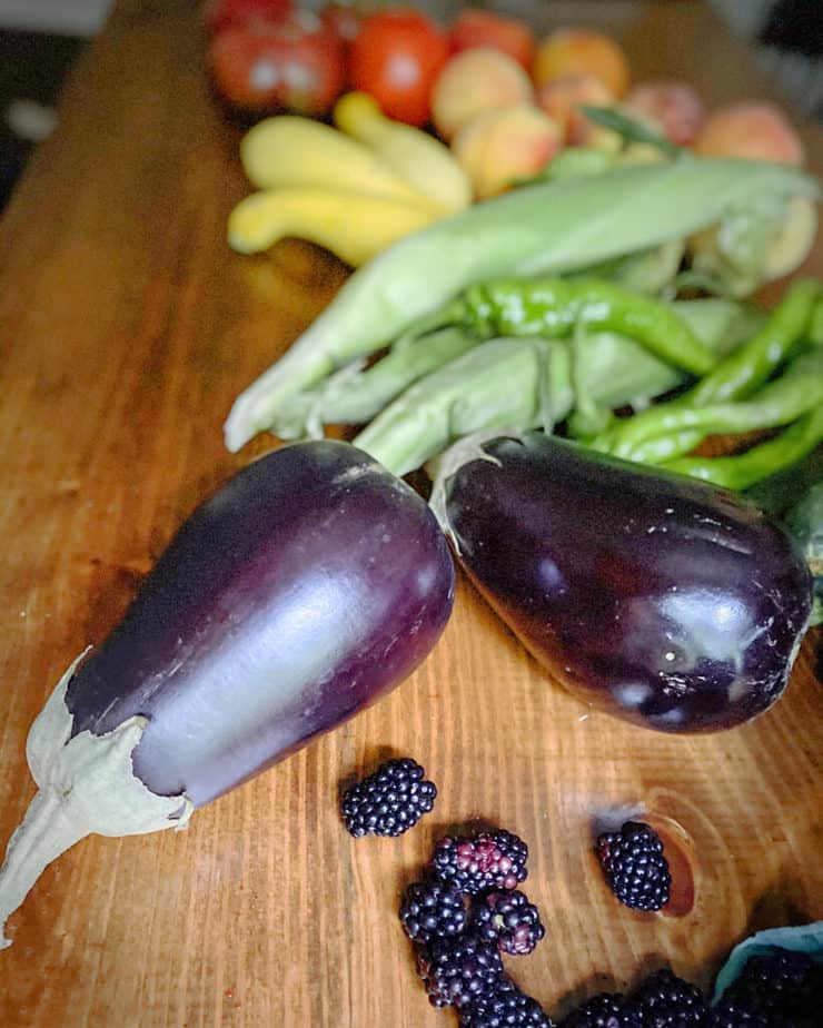 A photo of my farmer's market hall arranged in reverse ROYGBIV order, with blackberries and eggplant at the fore, followed by zucchini, mesilla peppers, corn in husks, yellow summer squash, peaches and finally tomatoes