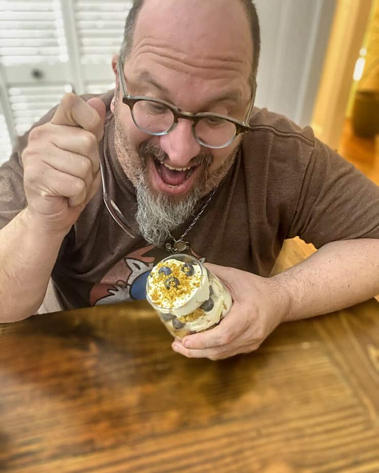 Handsome white bear in glasses excited to dig into a lemon blueberry ginger trifle at a wooden dinner table