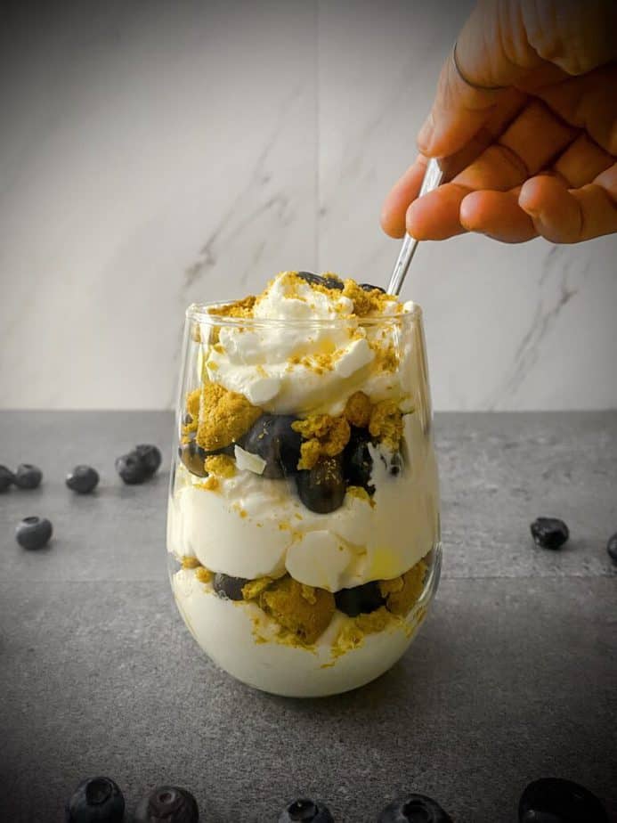 A hand reaching in for a spoonful of lemon blueberry ginger trifle