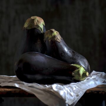 3 eggplants on a table as hero image for spicy ginger soy eggplant stirfry. photo credit don ricardo.