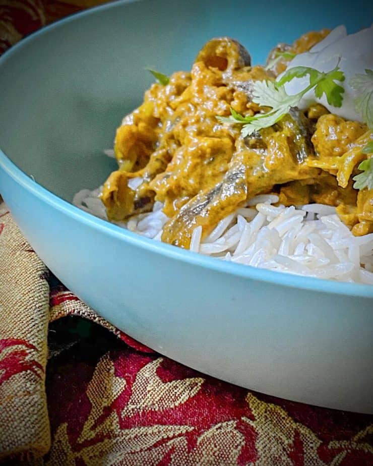 close up sideways shot of vegan tikka masala over rice in a turquoise bowl with plain yogurt and cilantro