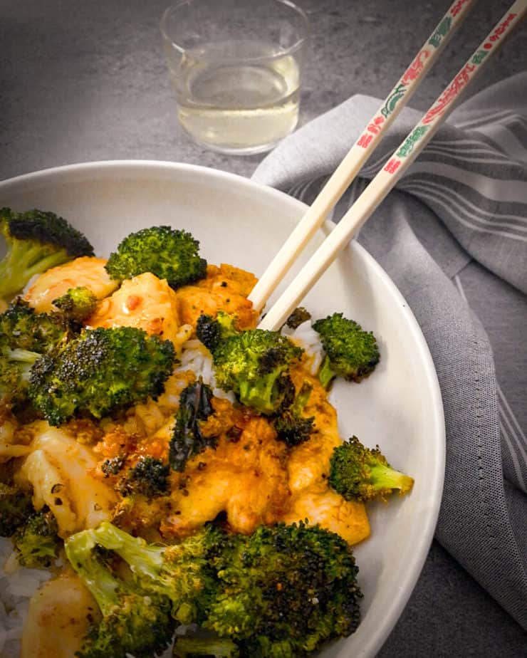 Close up of crispy orange chicken with broccoli and jasmine rice in a neutral bowl with chopsticks, a grey and white napkin and glass of white wine, made for my review of Home Chef