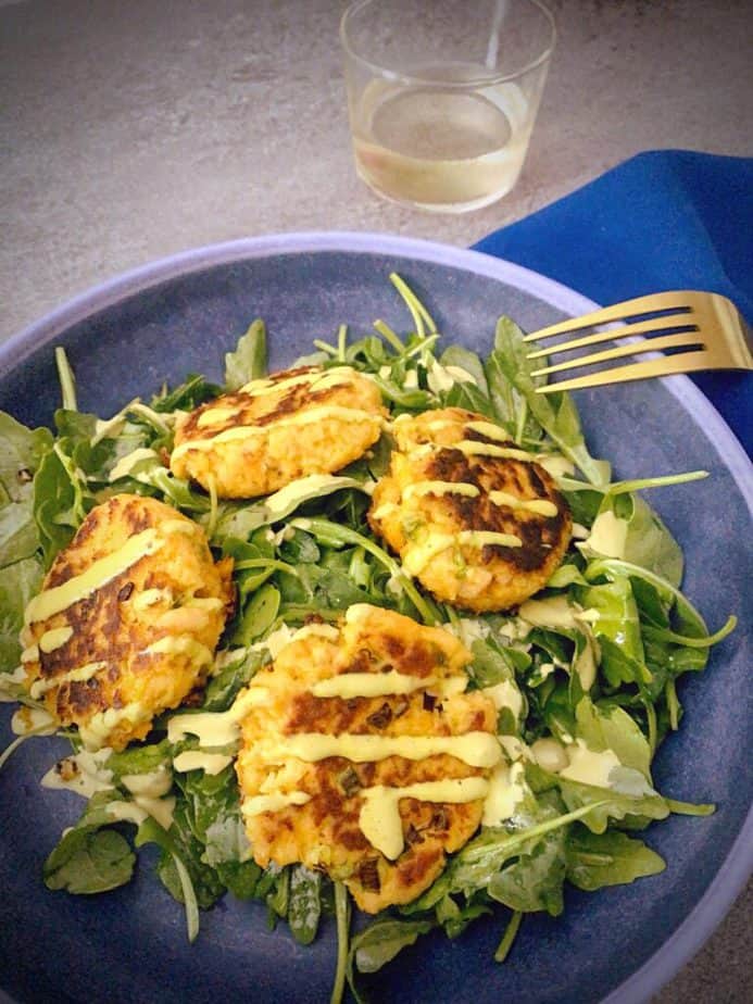 4 canned salmon and sweet potato fish cakes over a bed of arugula with  a gold fork and green sauce drizzle