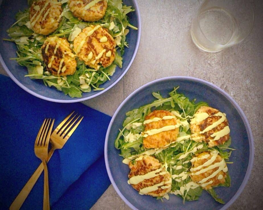 two salad bowls with sweet potato salmon cakes over arugula with peruvian green sauce drizzle and gold forks