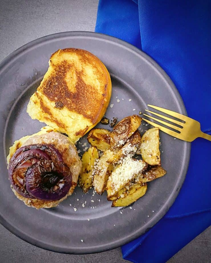 overhead shot of pork burger on a toasted bun with balsamic mayonnaise, charred red onion and garlic parmesan potato wedges on a dark grey plate with a gold fork and royal blue linen napkin from my review of blue apron