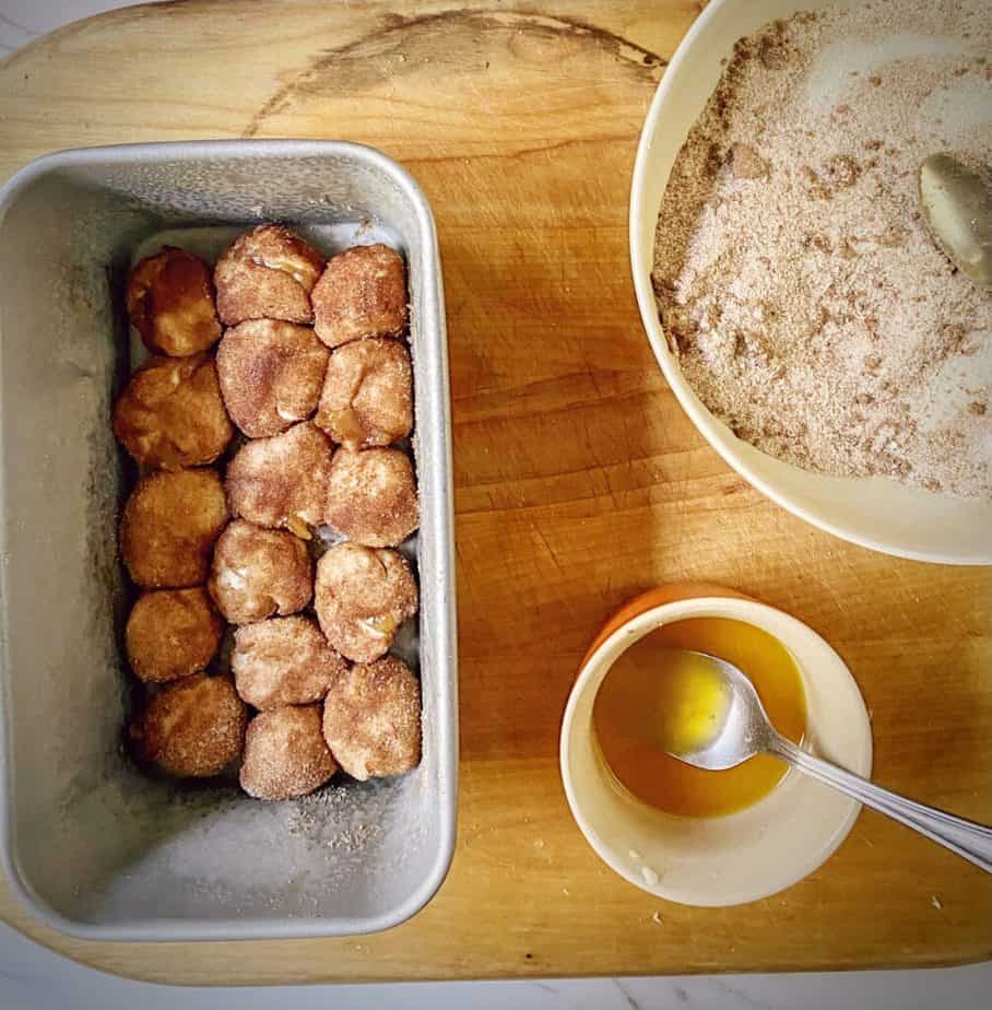 cinnamon sugar dipped dough balls in a loaf tin on a wooden cutting board with leftover butter and cinnamon sugar on the side