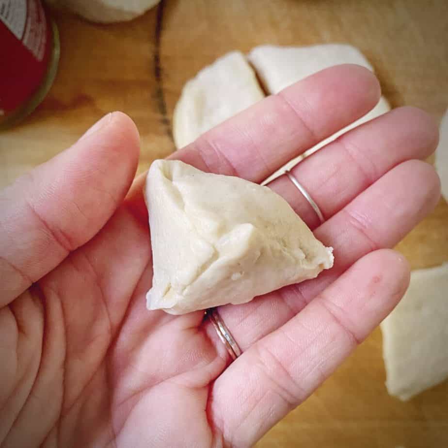 biscuit dough that has been filled with cinnamon bun spread pinched shut into a little pyramid