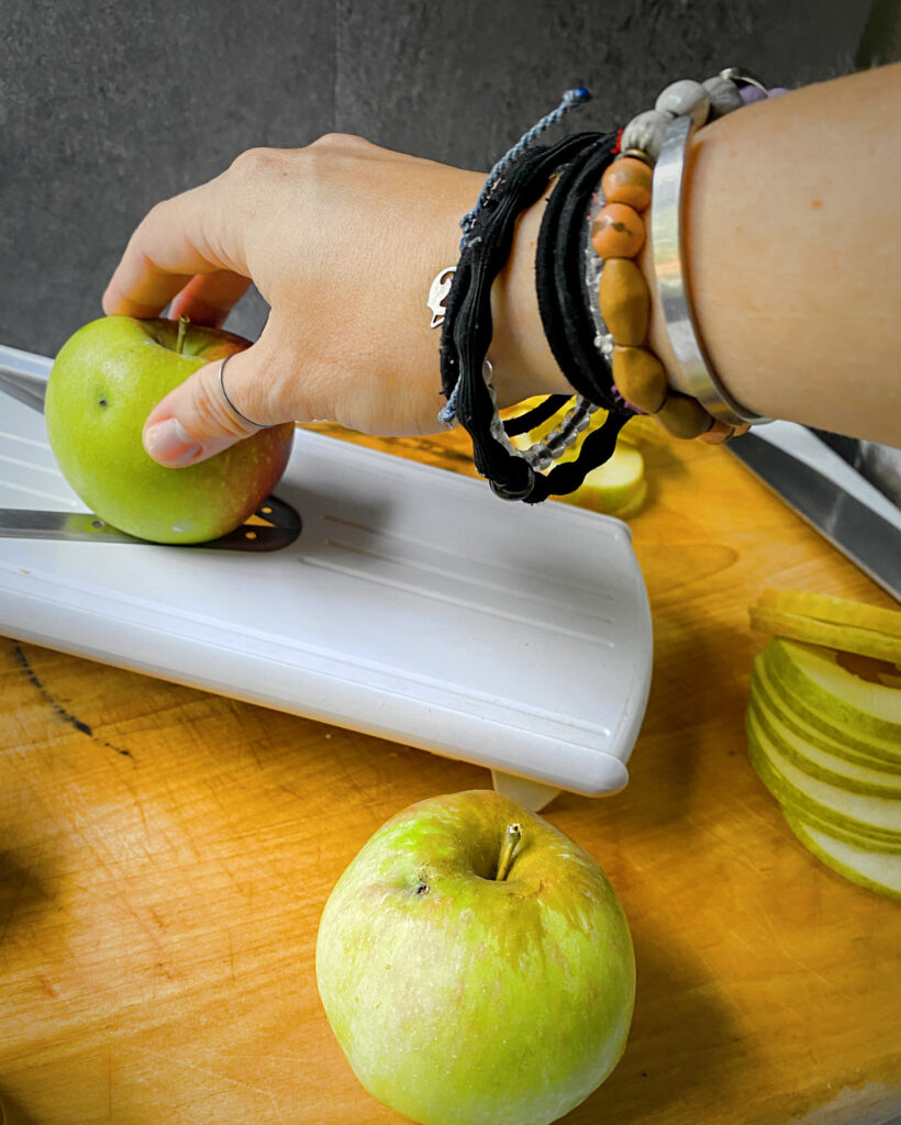 hand slicing apples on a mandoline on a wooden surface