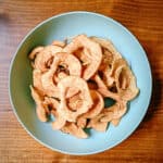 finished homemade apple chips in a turquoise bowl on a dark wooden background
