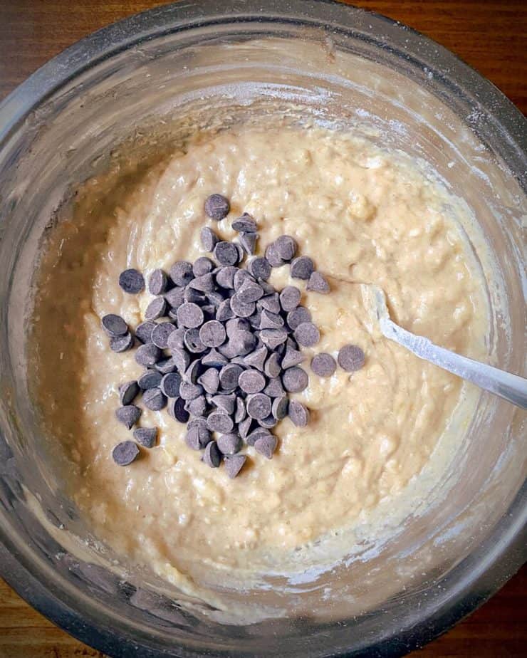 pile of chocolate chips on top of banana breakfast bar batter in a metal bowl 
