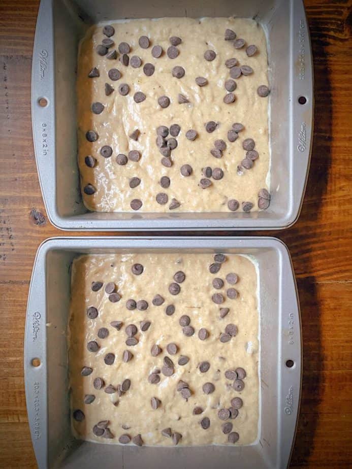 two 8 x 8 baking tins filled with healthy banana chocolate chip breakfast bar batter and sprinkled with chocolate chips on top on a wooden table