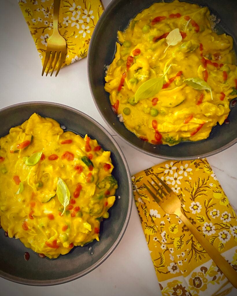 overhead shot of butternut apple soup turned into a quick weeknight curry with rotisserie chicken, green beans, peas, zucchini, broccoli in grey pasta bowls over cauliflower rice with yellow floral napkins and gold forks