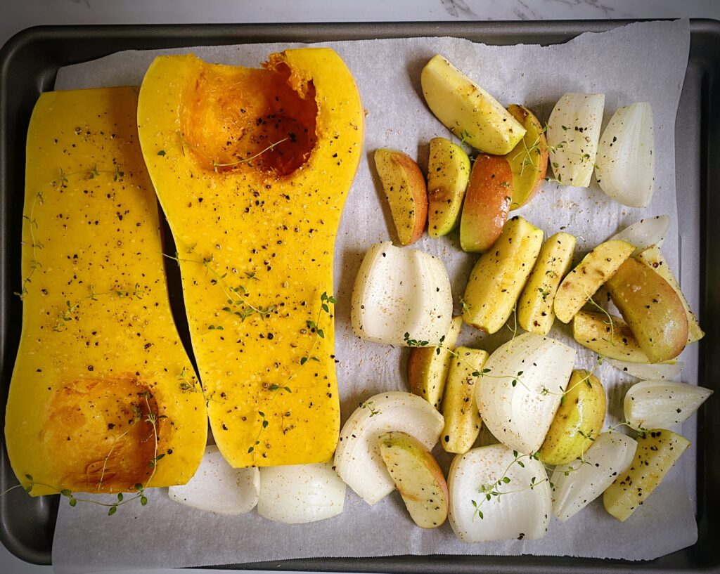 halved butternut squash, apple and onion wedges seasoned with salt, pepper and olive oil on a sheet pan ready for baking