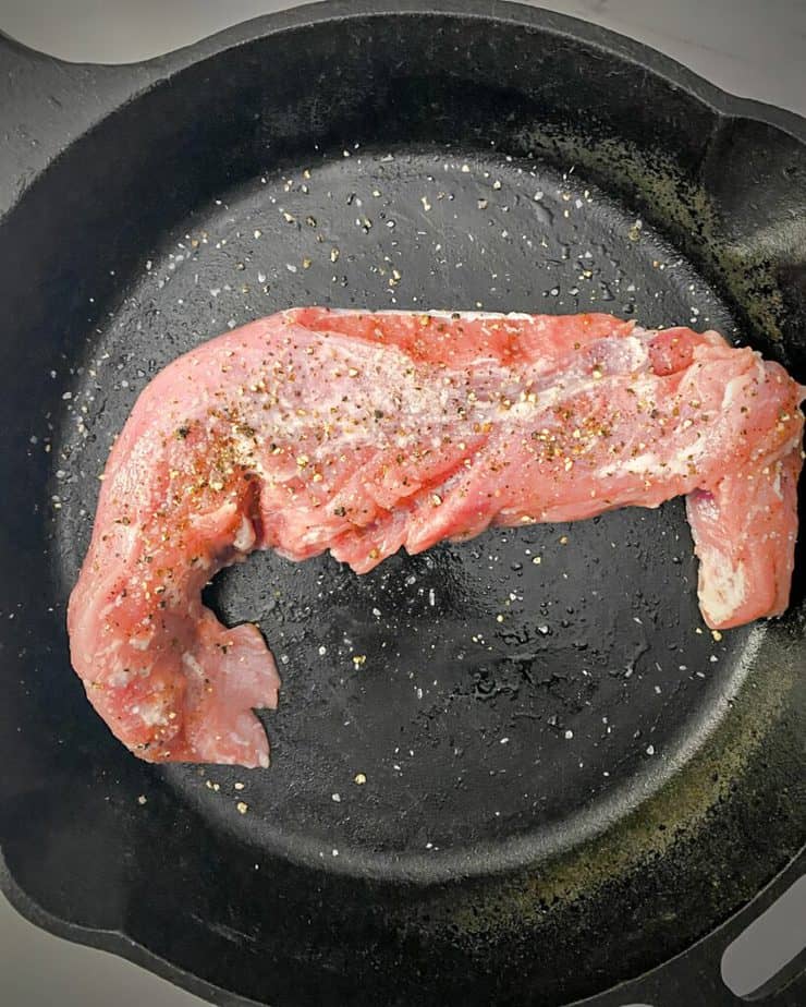 raw pork tenderloin in a cast iron skillet with salt and pepper
