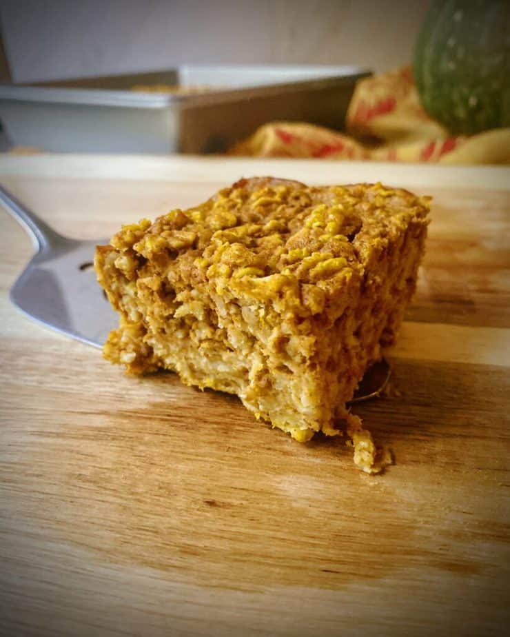 closeup of a square of pumpkin pie baked oatmeal on a serving spatula on top of a wooden cutting board 