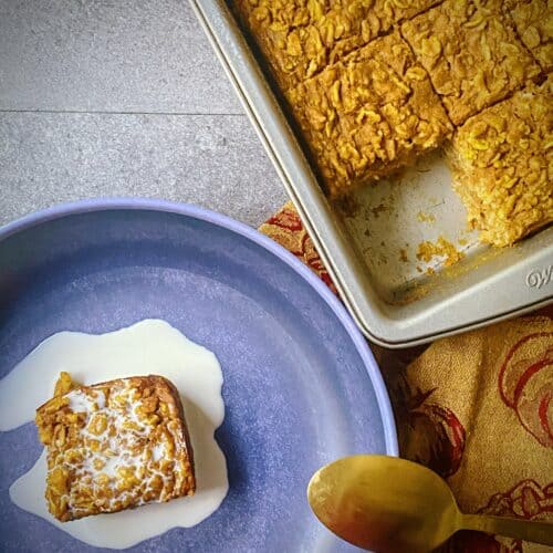 overhead shot of one slice of pumpkin baked oatmeal covered with cream in a blue bowl next to baking tin