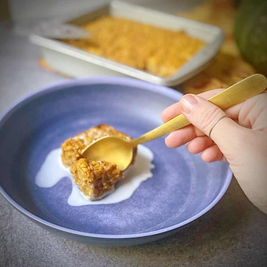 hand holding a gold spoon to take a bite of pumpkin pie baked oatmeal topped with cream in a blue pasta bowl 