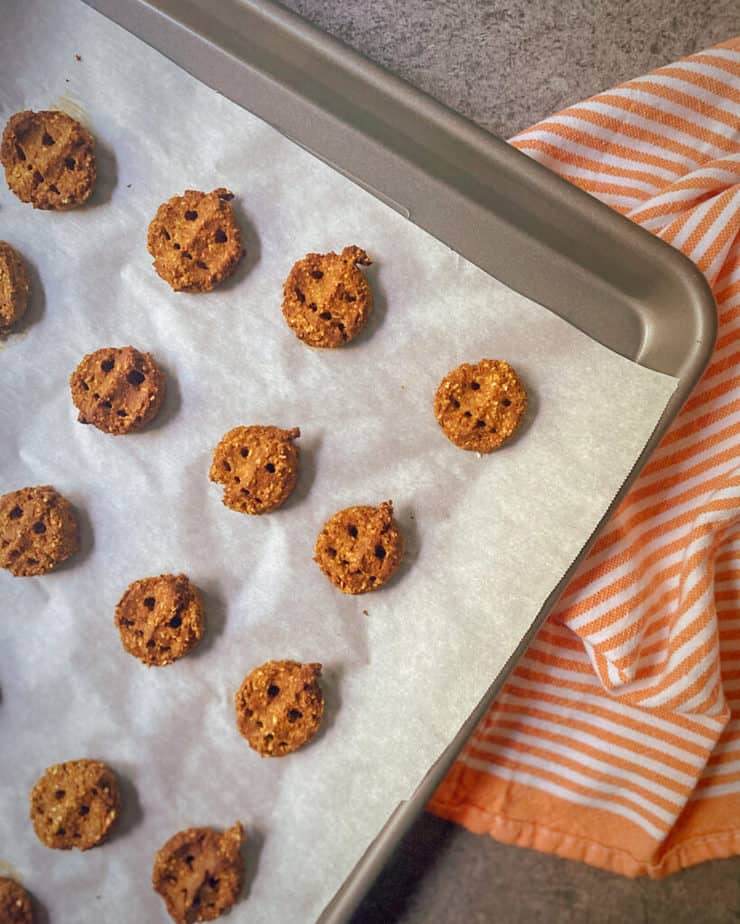 pumpkin peanut dog treats on a parchment lined cookie sheet with an orange and white striped tea towel