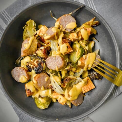 sheet pan sausage and veggies in a grey pasta bowl on a grey napkin with gold fork