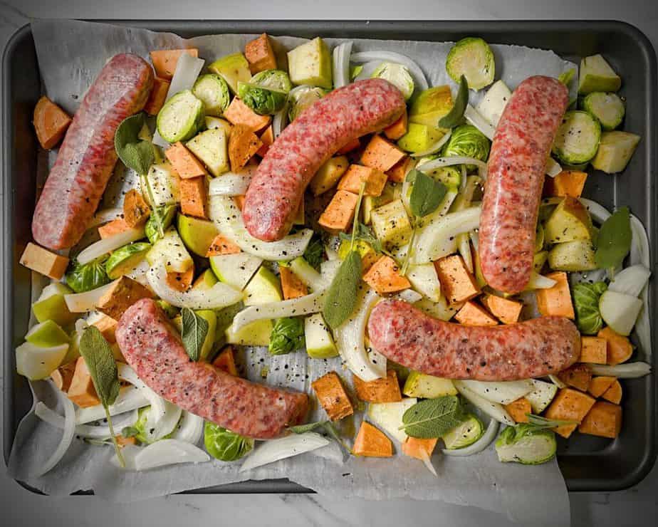 sausages on top of chopped veggies on a sheet pan prior to baking