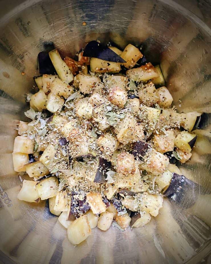 eggplant chunks in a metal bowl with olive oil, mint, oregano, salt and pepper