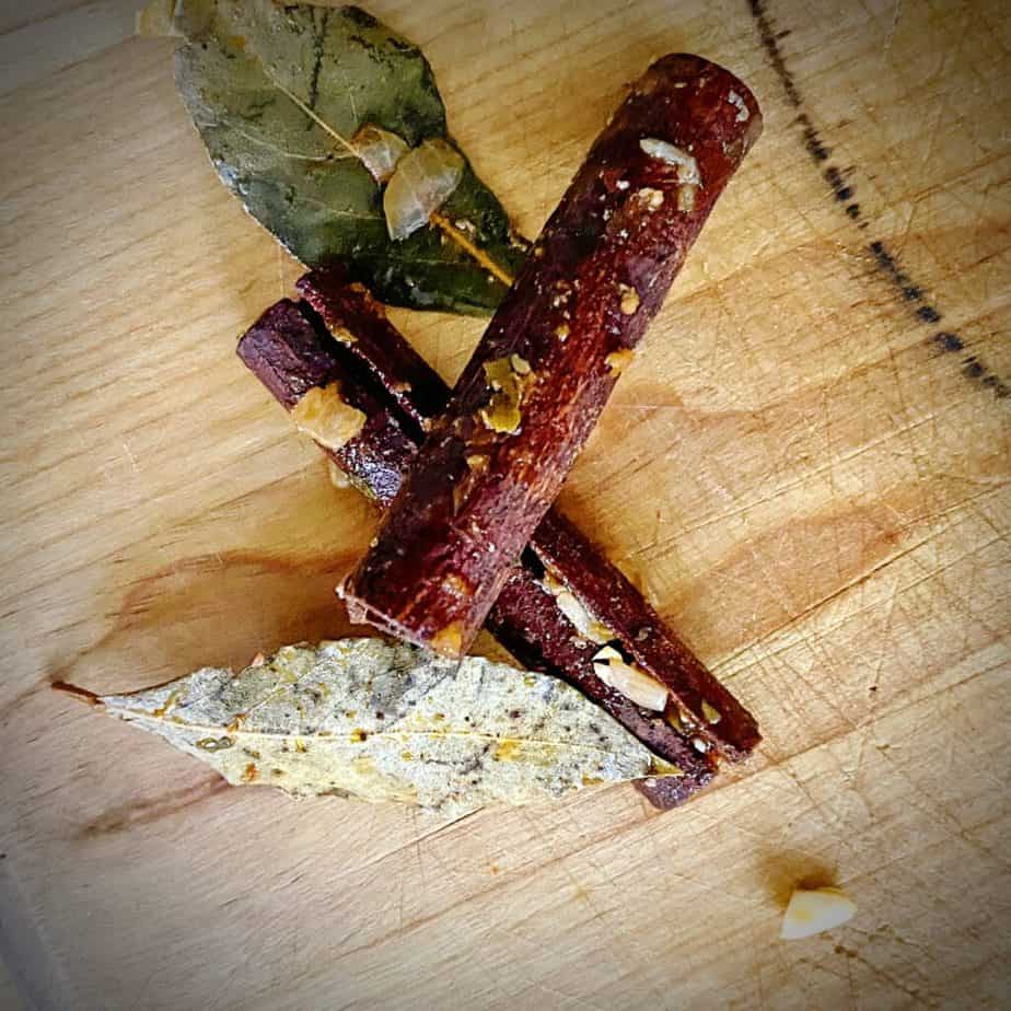 two bay leaves and cinnamon sticks after being removed from tomato lamb bolognese on a wooden cutting board