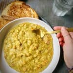 hand with a gold spoon dipping into a bowl of split pea and ham soup with a glass of sparkling water and a smoked gouda and ham grilled cheese