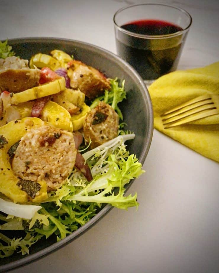 close up shot of pork sausage, delicata squash and frissée salad in a grey pasta bowl with a saffron yellow napkin and gold fork from my first meal for the sun basket review