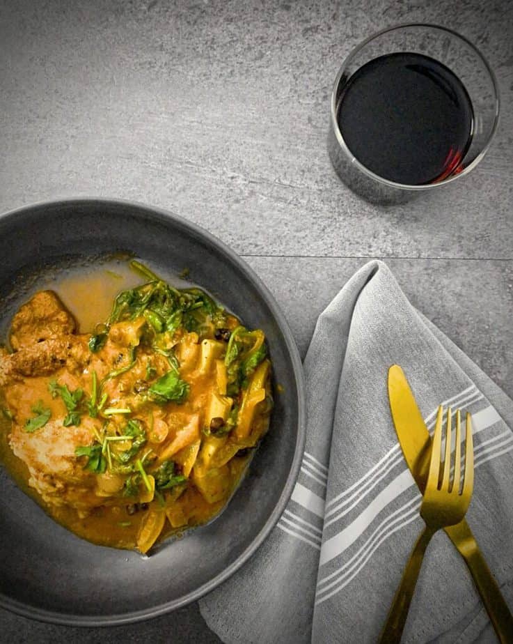 close up of chicken tagine in a grey pasta bowl with gold fork and knife and a grey and white striped napkin