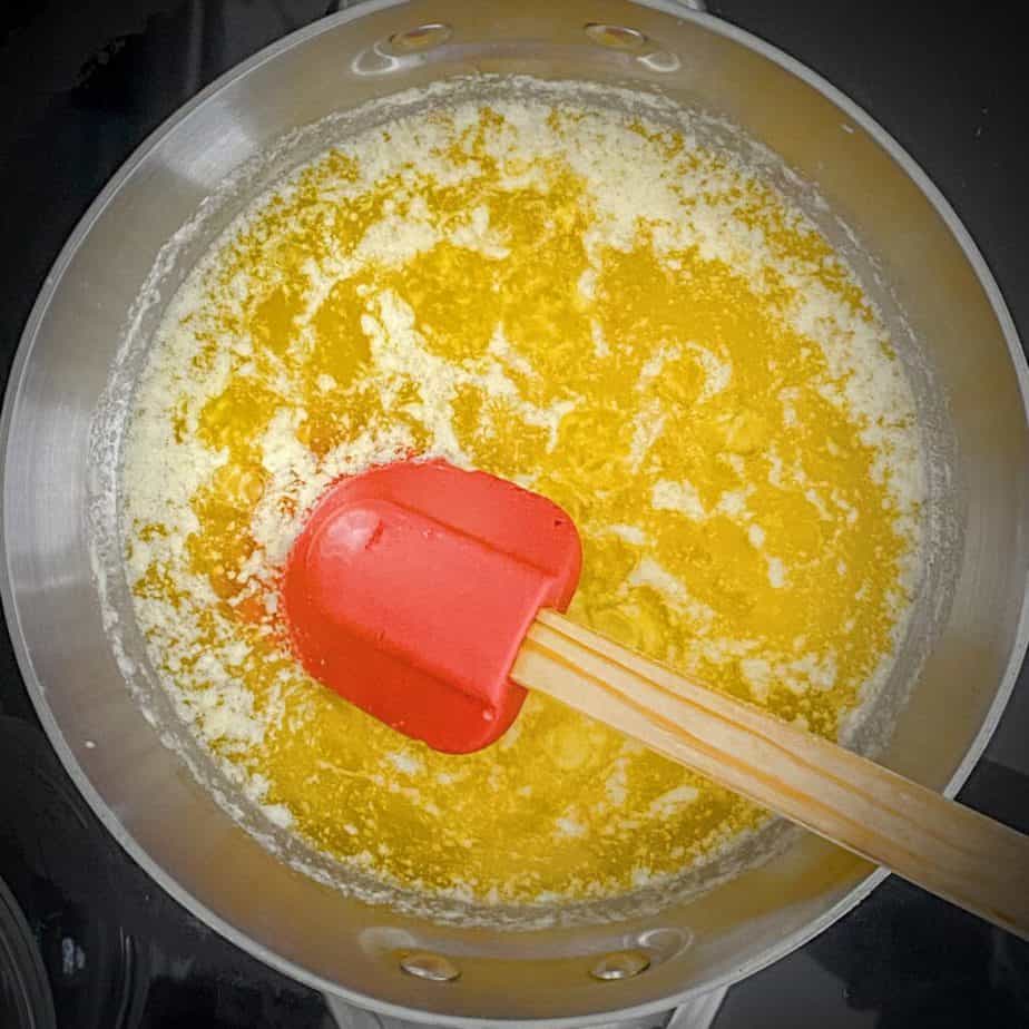 first step of browning butter in a saucepan - milk solids floating to the top of the ghee