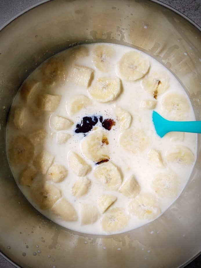 bananas, milk and vanilla paste mixed together in a saucepan with a turquoise silicone spatula