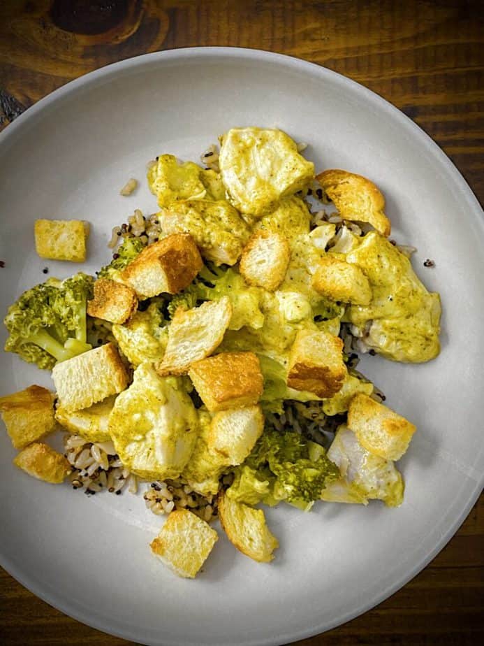 chicken divan casserole served over rice in a tan pasta bowl and sprinkled with baked golden croutons