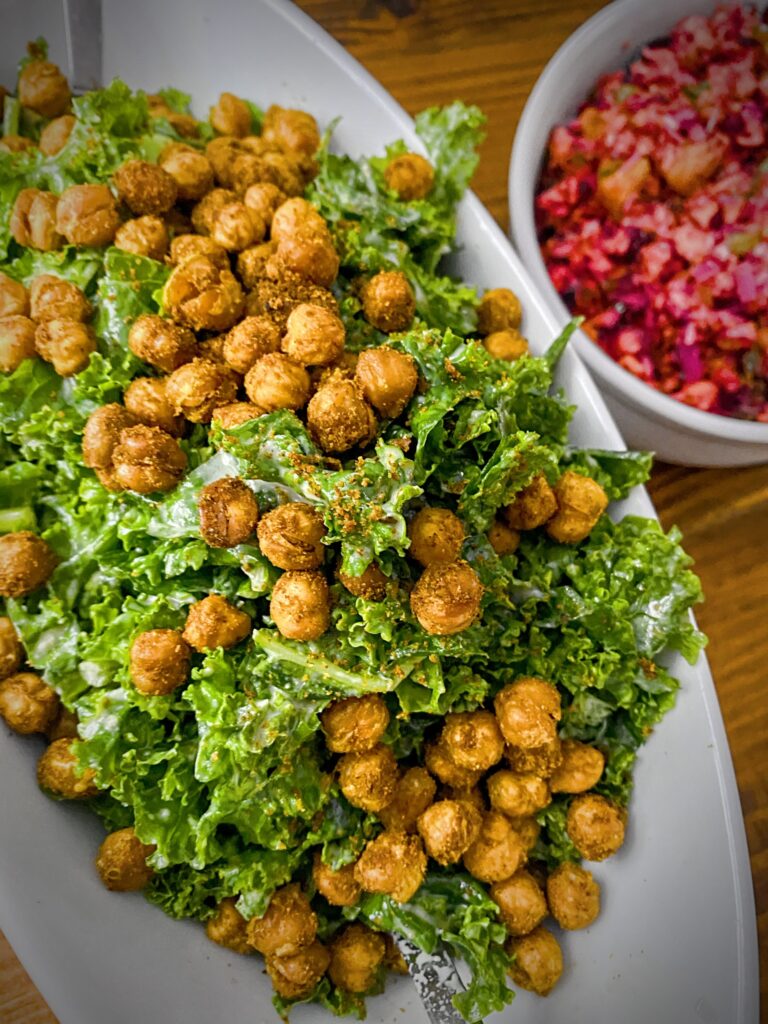 kale salad with tandoori roasted chickpeas in an oblong white dish on a wooden table with a bowl of cranberry relish to the side