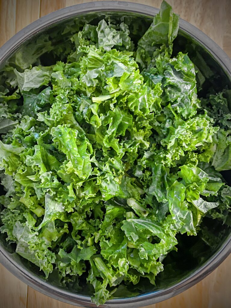 raw kale drizzled with lemon juice and olive oil in a mixing bowl 