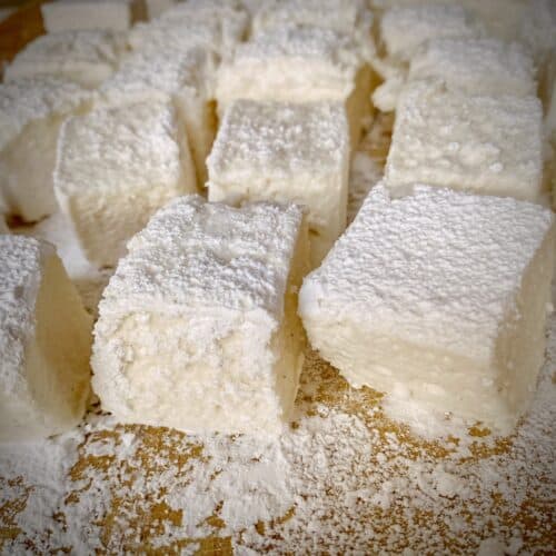 homemade vanilla marshmallows dusted in powdered sugar and cornstarch on a wooden cutting board