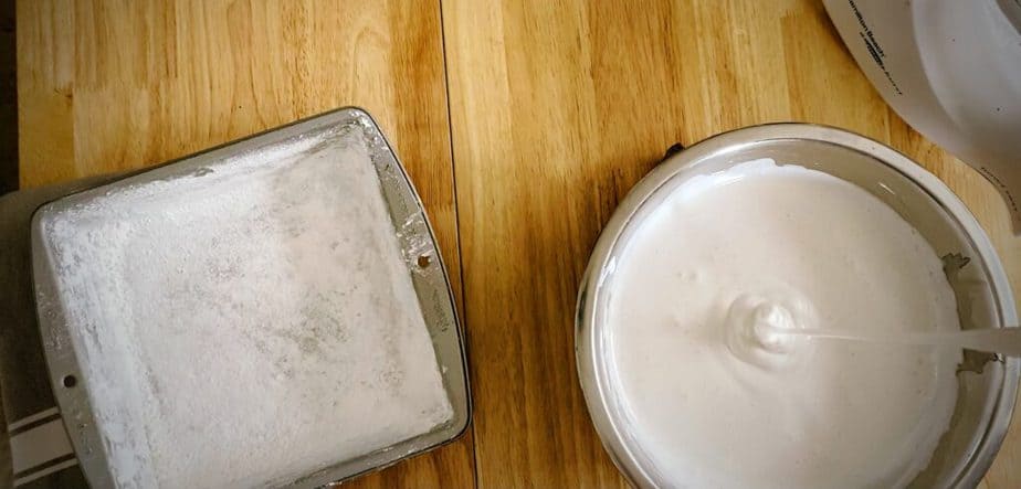 overhead shot showing finished consistency of homemade marshmallow mix next to corn starch coated 8x8 cake tin