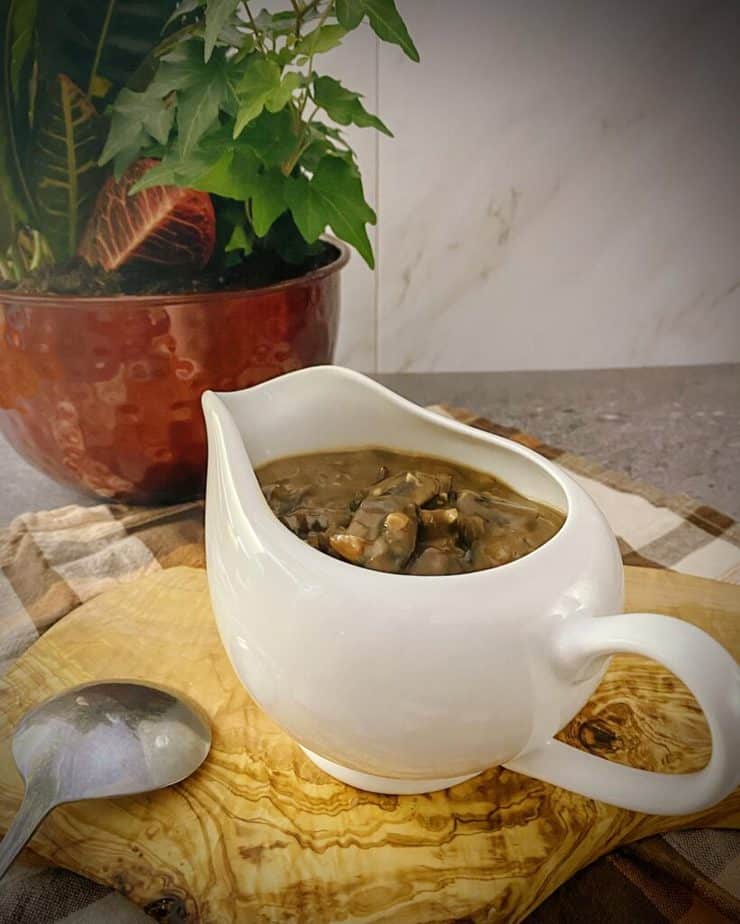 mushroom gravy in a white gravy boat on an olive wood board with a copper planter filled with an autumn arrangement behind it