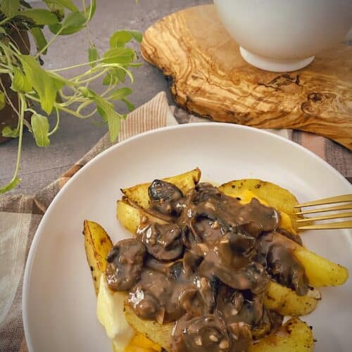poutine with mushroom gravy in a white pasta bowl with a gravy boat and a sage plant