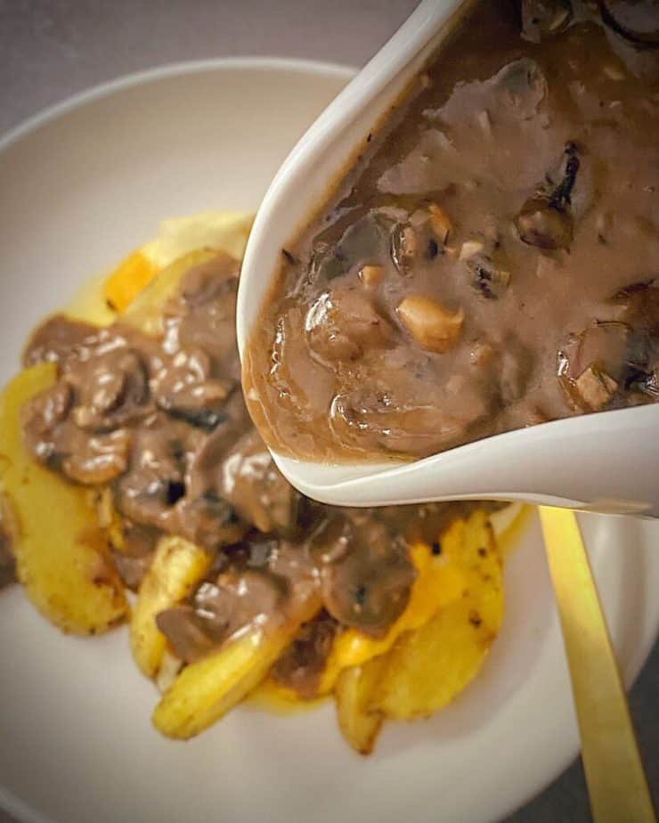 gravy boat with mushroom gravy being poured onto a plate of poutine