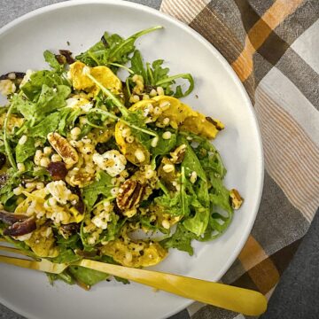 overhead shot of delicata squash harvest salad in a white pasta bowl with a pale orange, brown and white plaid napkin and a glass of white wine.